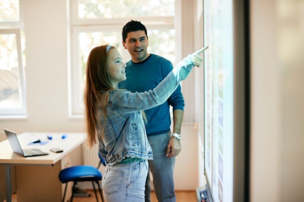 High school student using smart board with her teacher in the classroom.