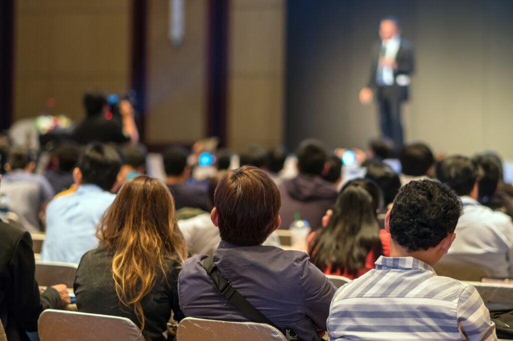 Rear side of Audiences sitting and listening the speackers on the stage in low light conference hall